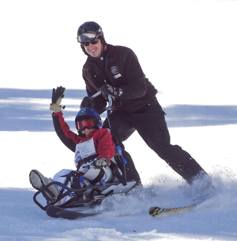 Ray LoCascio skiing alongside a smiling young athlete in an adaptive sit-ski